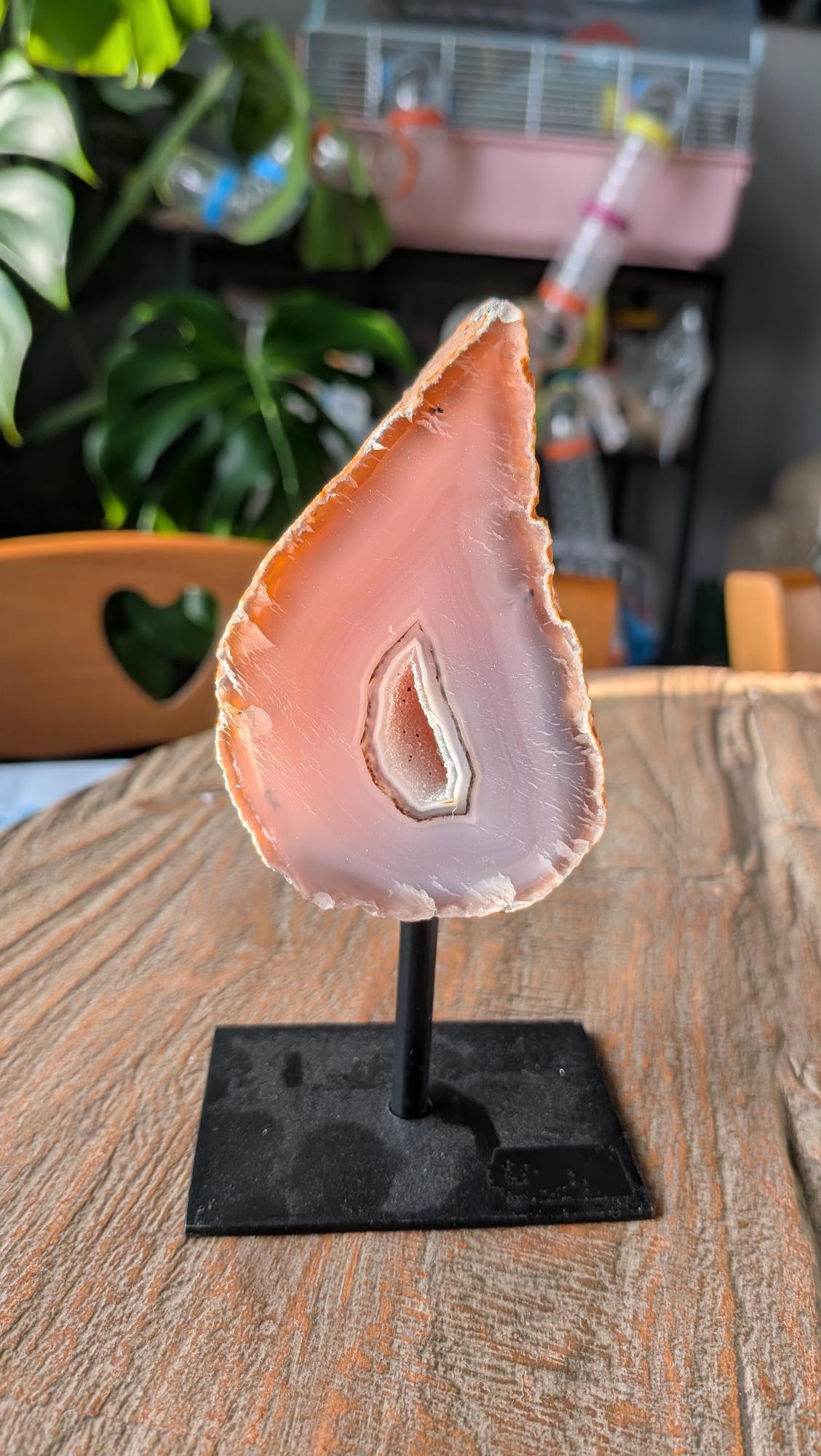 Een gepolijste agaatgeode met een kristallen kern, gemonteerd op een strakke zwarte metalen standaard op een houten tafel.