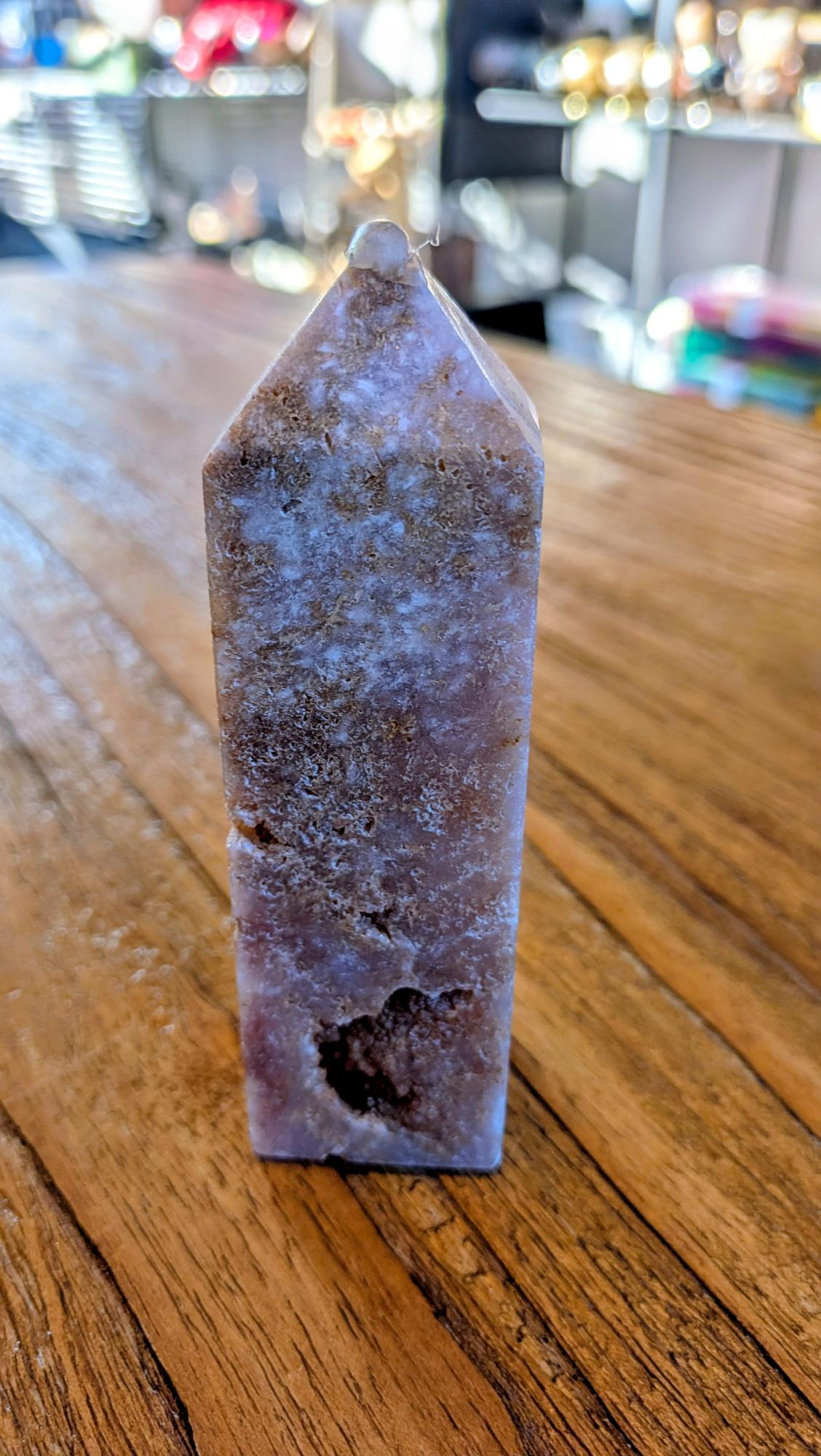 "Zijaanzicht van een gepolijste roze amethist punt met natuurlijke patronen in roze en aardetinten op een houten tafel."