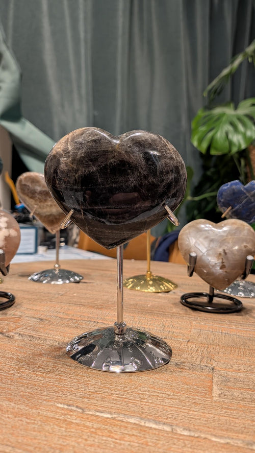 "Gepolijst hart van zwarte maansteen met subtiele zilveren glans, gepresenteerd op een luxe zilverkleurige metalen standaard voor interieurdecoratie."