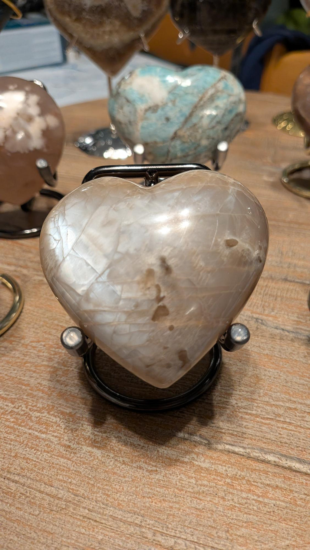 "Handgeslepen Grijze Maansteen hart van 157 gram op een metalen standaard, met zichtbare zilveren adularescentie."