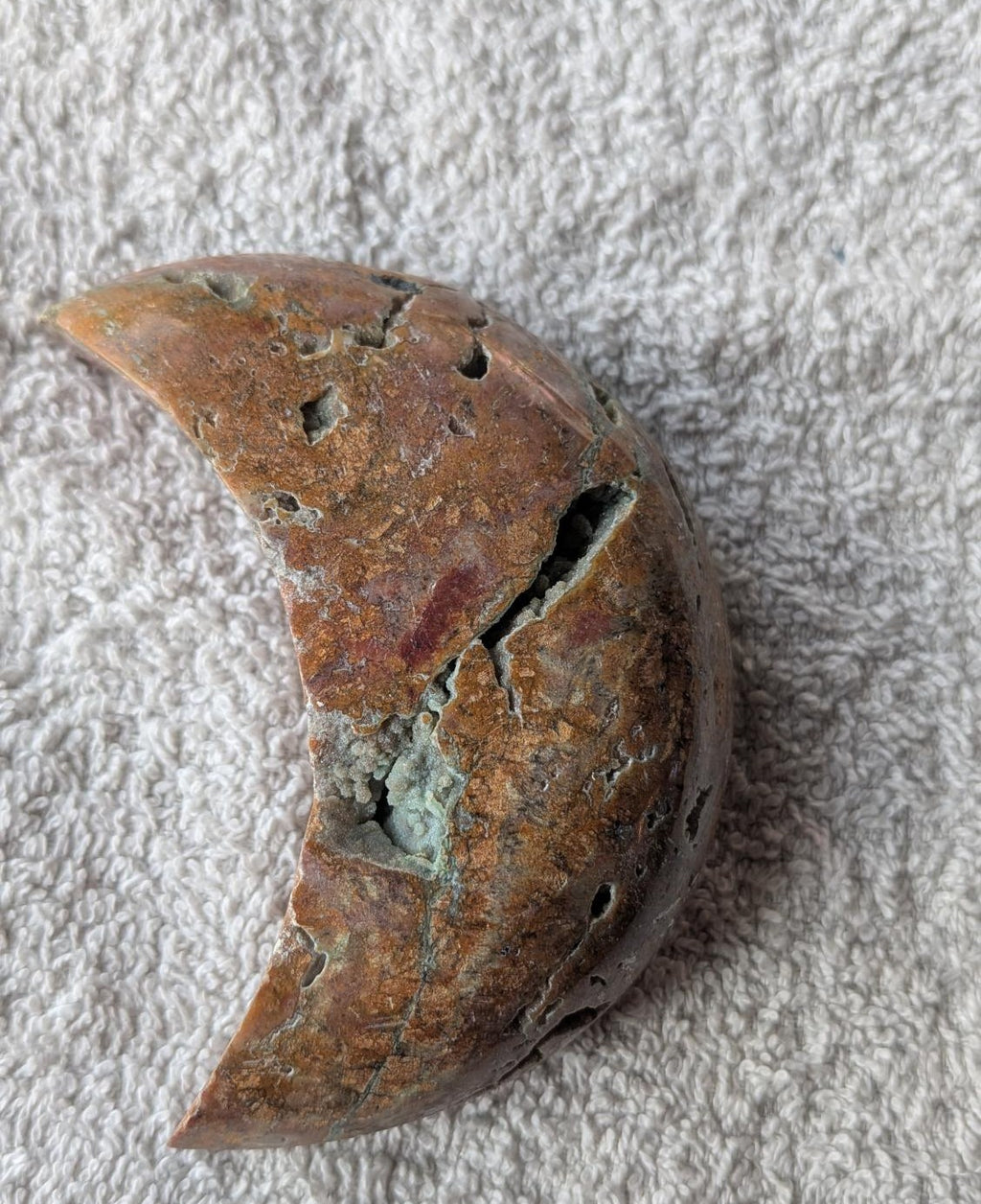 Handgeslepen Oceaan Jaspis halve maan met bruine tinten en diepe natuurlijke kristalholtes op een witte achtergrond.