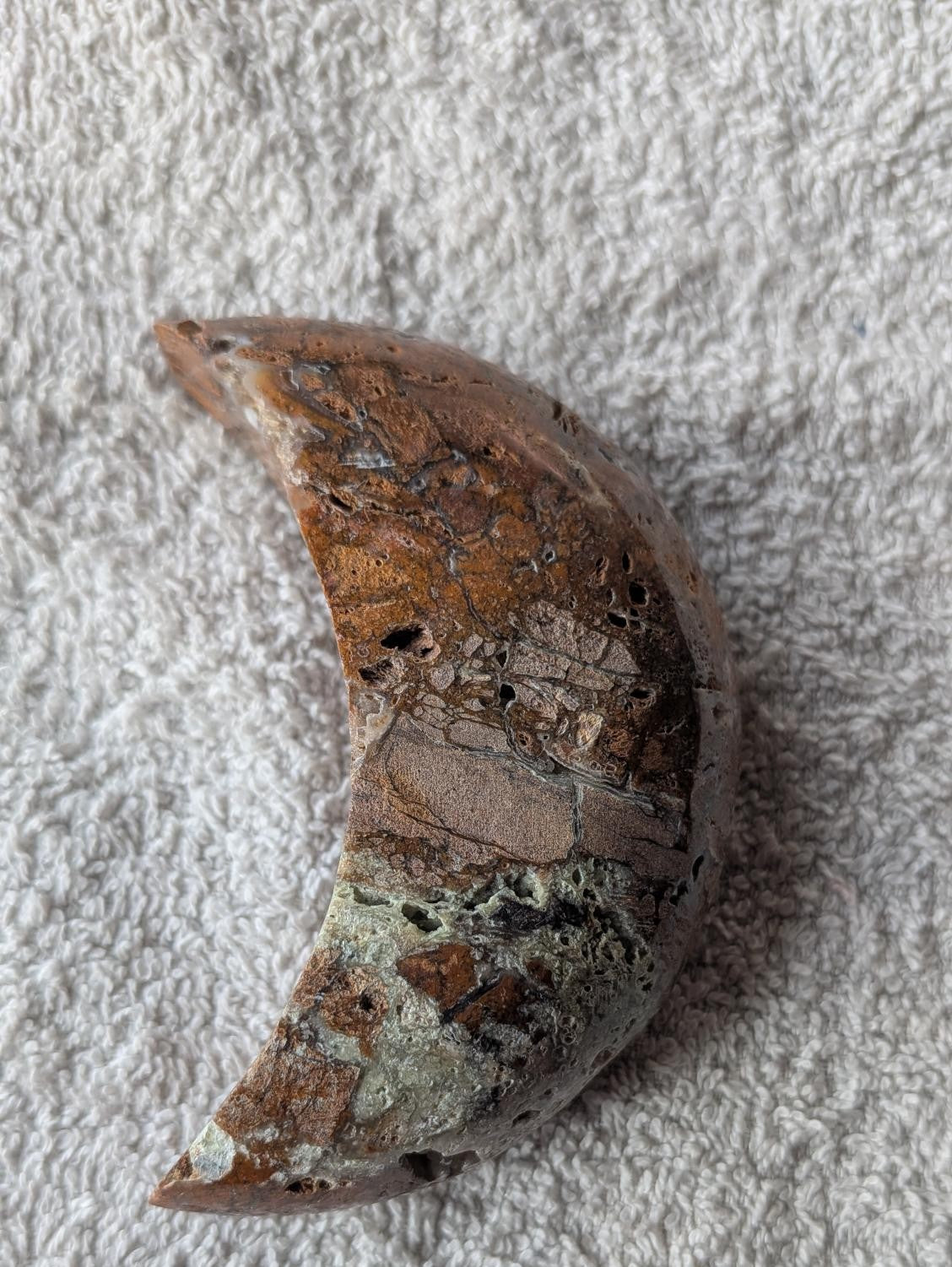 Handgeslepen halve maan van Oceaan Jaspis in bruin- en groentinten met natuurlijke gaatjes en kristalstructuren.