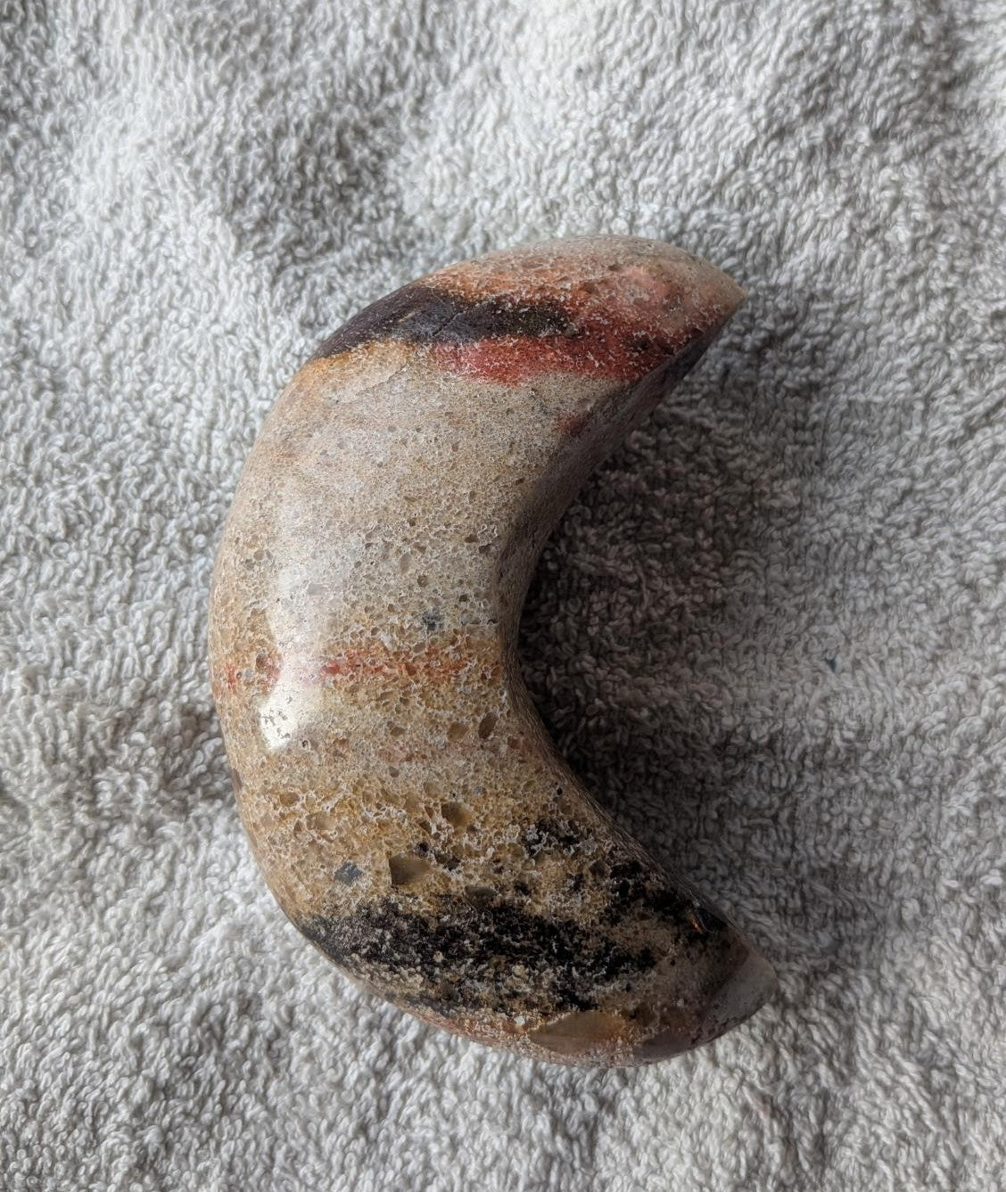 Handgeslepen halve maan van Landschapsjaspis met aardse patronen van bruin, beige en zwart, liggend op een witte achtergrond.