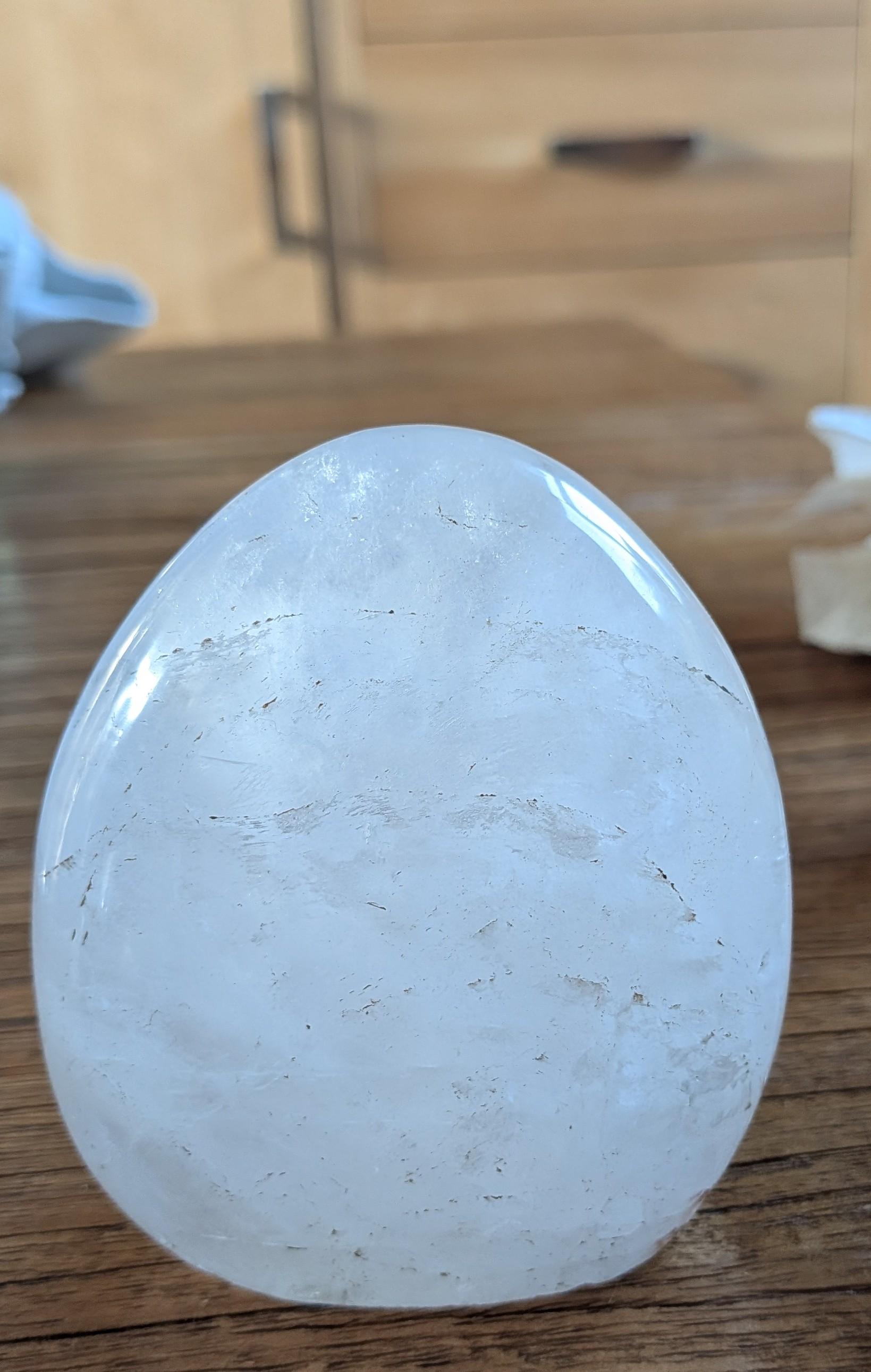 Handgepolijste bergkristal freeform van 464 gram met heldere transparantie en natuurlijke witte sluiers, staand op een houten tafel.