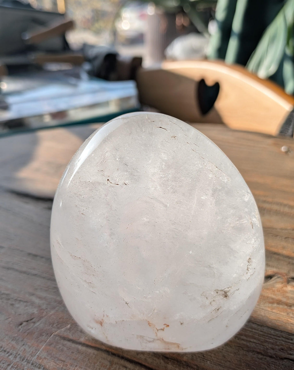 Handgepolijste bergkristal freeform van 464 gram met heldere transparantie en natuurlijke witte sluiers, staand op een houten tafel.