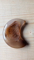 Handgeslepen bruine Agaat in de vorm van een maan met een sprankelende kristallen druzy holte op een houten ondergrond.
