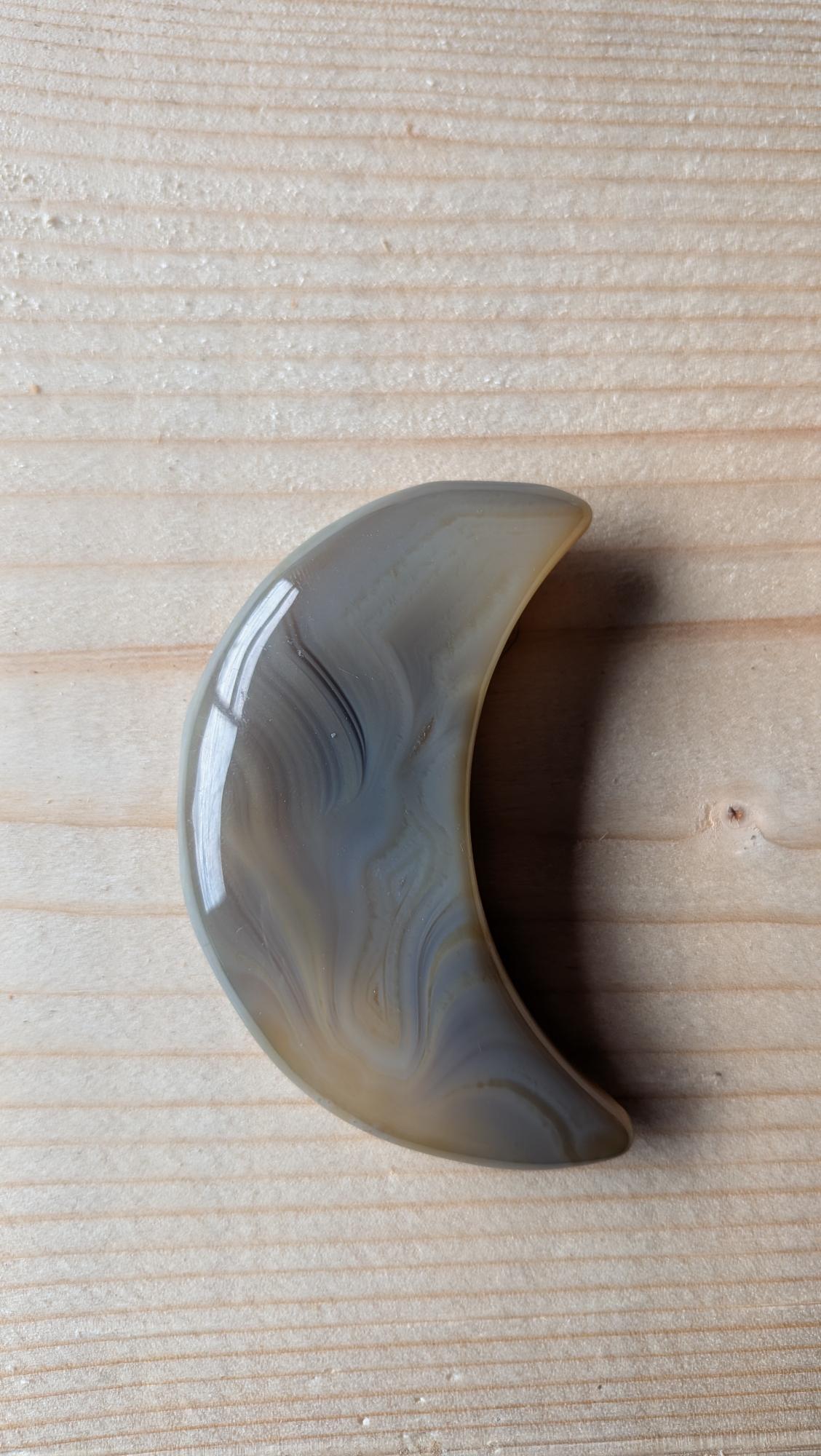 Handgeslepen grijze Agaat edelsteen in de vorm van een halve maan met natuurlijke gelaagde patronen, 7 centimeter groot.