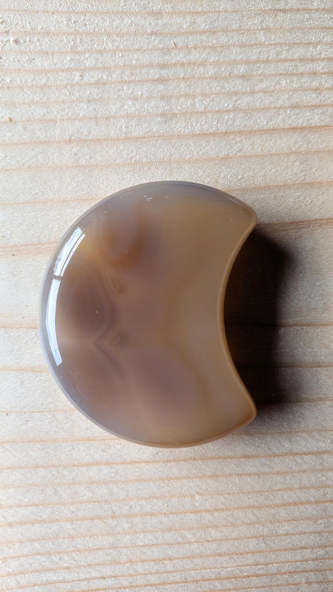 Handgeslepen volle Agaat maan in warme bruin- en grijstinten, 5,5 centimeter groot, gefotografeerd op een houten ondergrond.