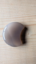 Een massief gepolijste grijze Agaat edelsteen in de vorm van een halve maan, 5 centimeter groot, gefotografeerd op een lichte houten ondergrond.