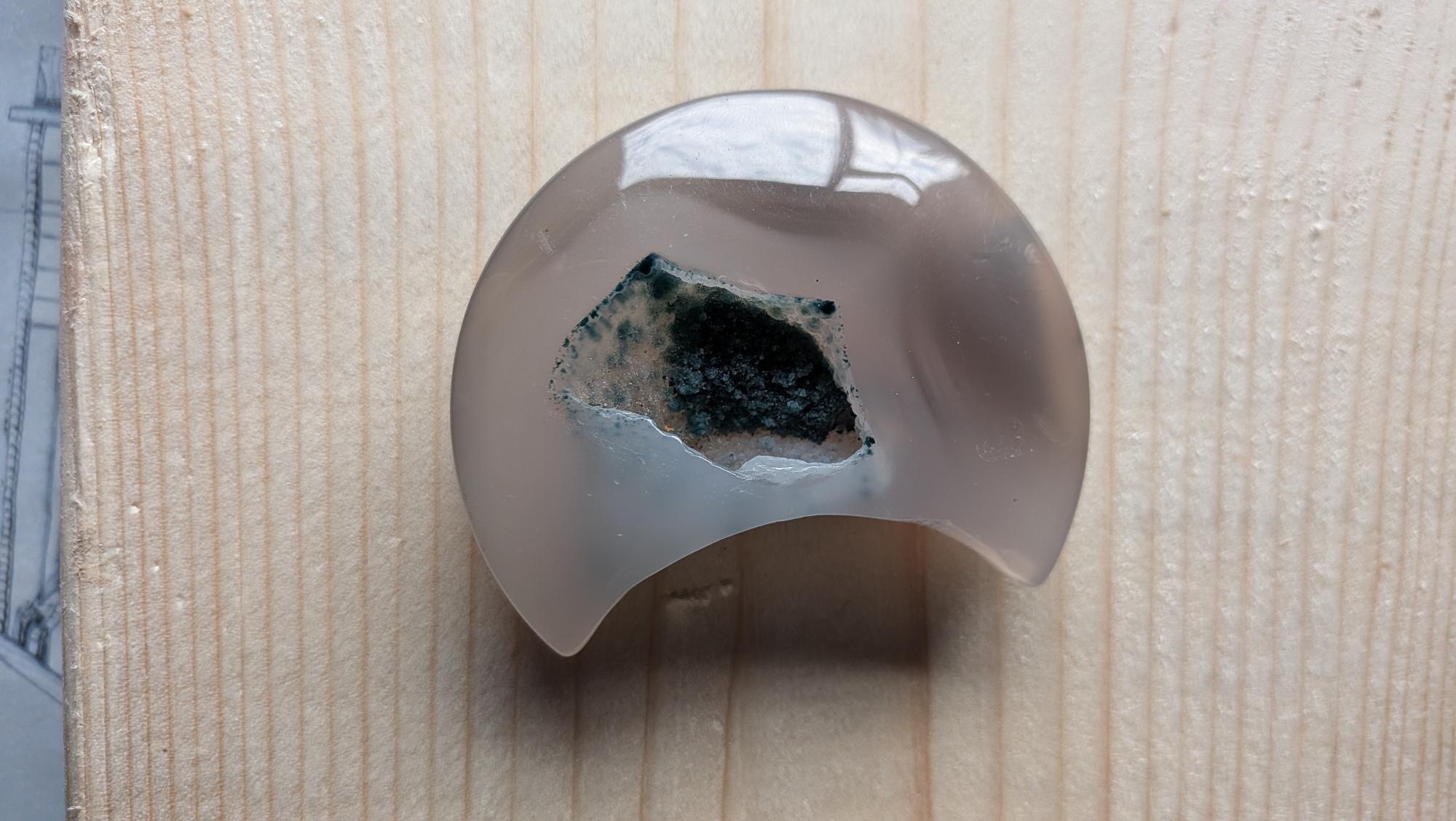 Handgeslepen lichtgrijze Agaat edelsteen in maanvorm met een grote centrale kristalgeode gevuld met donkergroene mos-achtige kristallen.