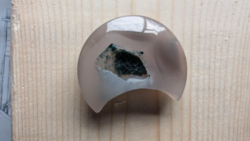 Handgeslepen lichtgrijze Agaat edelsteen in maanvorm met een grote centrale kristalgeode gevuld met donkergroene mos-achtige kristallen.