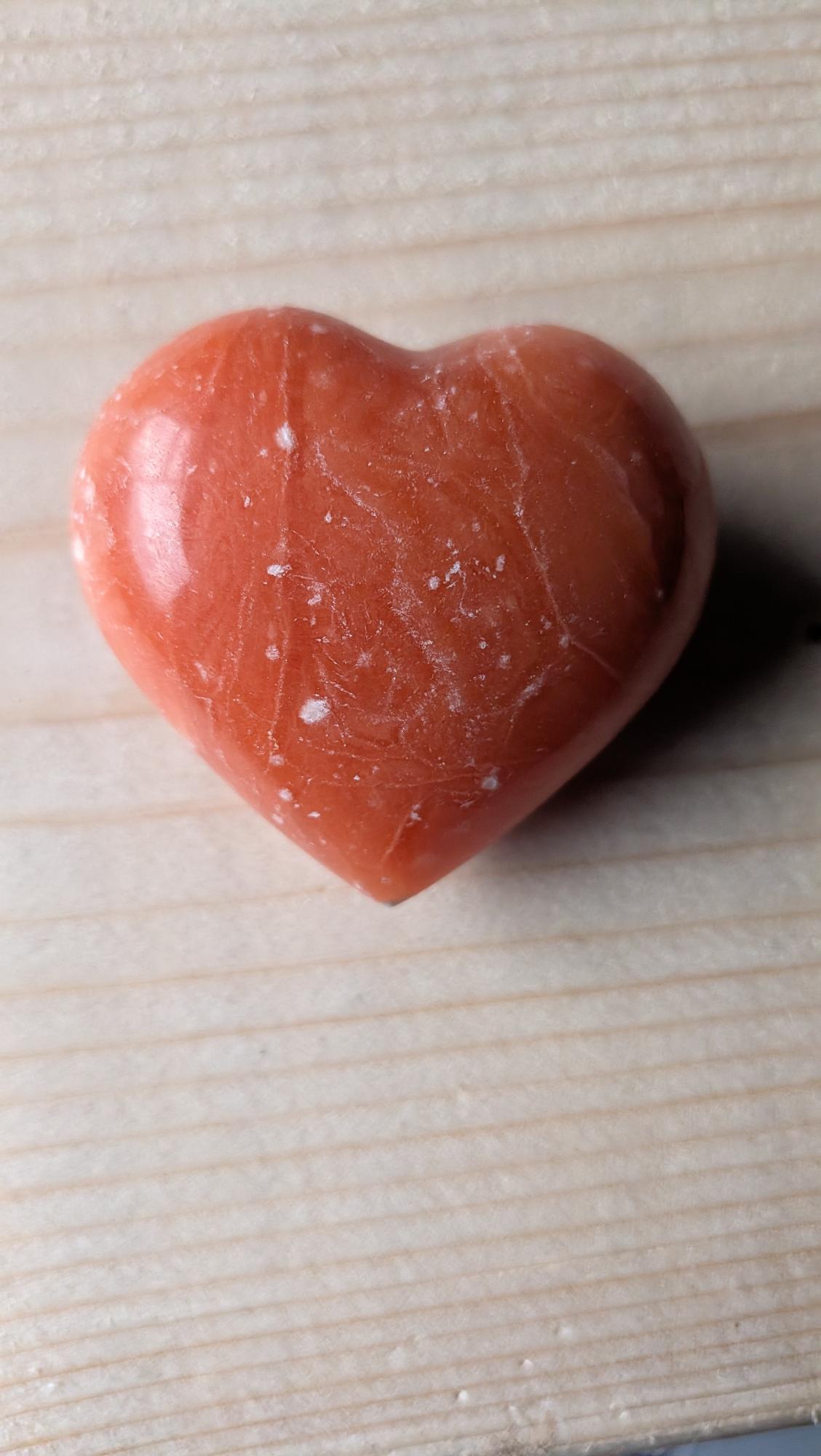 Een gepolijst edelsteen hart van Oranje Calciet met witte aders, 5 centimeter groot, gefotografeerd op een houten ondergrond.
