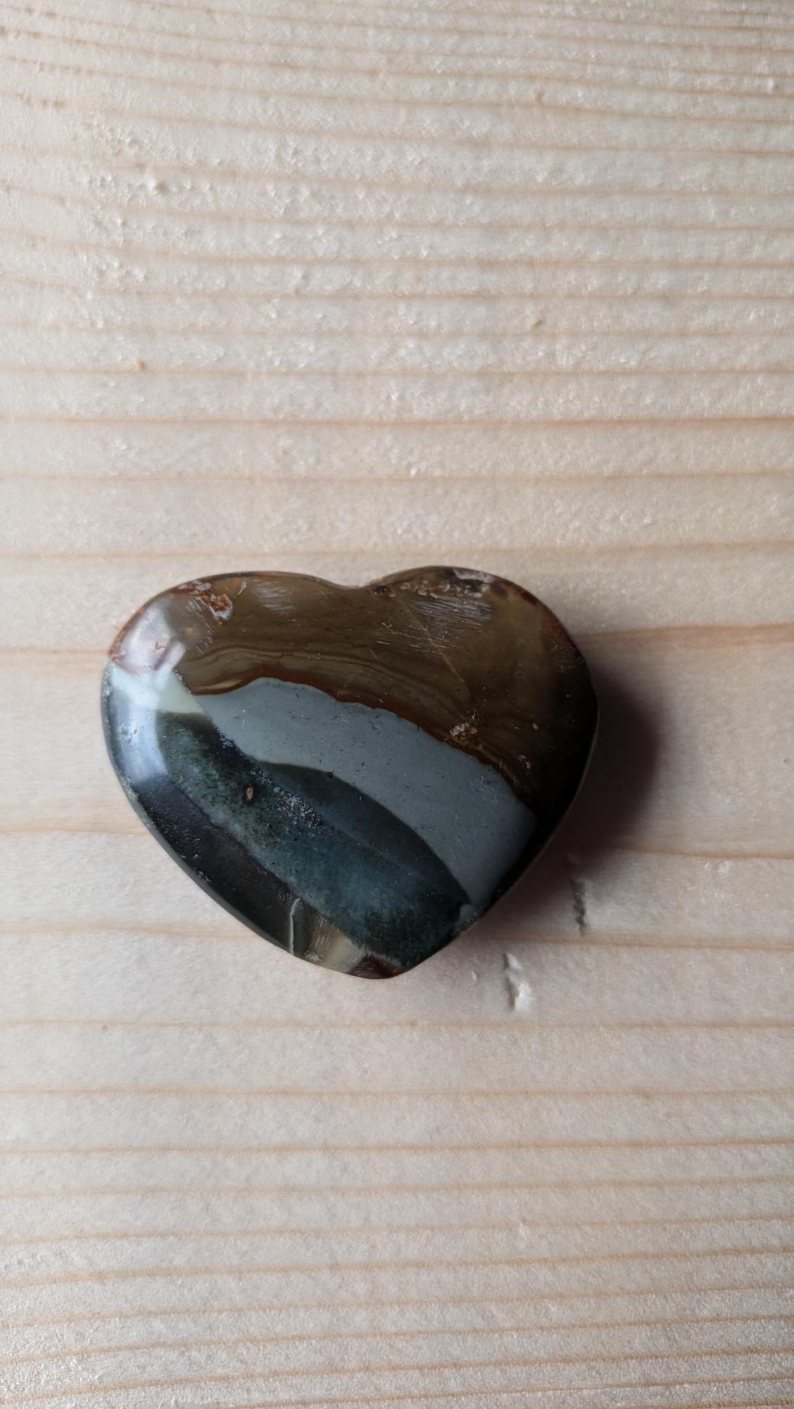 Een gepolijst Oceaan Jaspis hart met duidelijke lagen van bruin, grijsblauw en donkergroen, 4,5 cm groot, op een houten ondergrond.