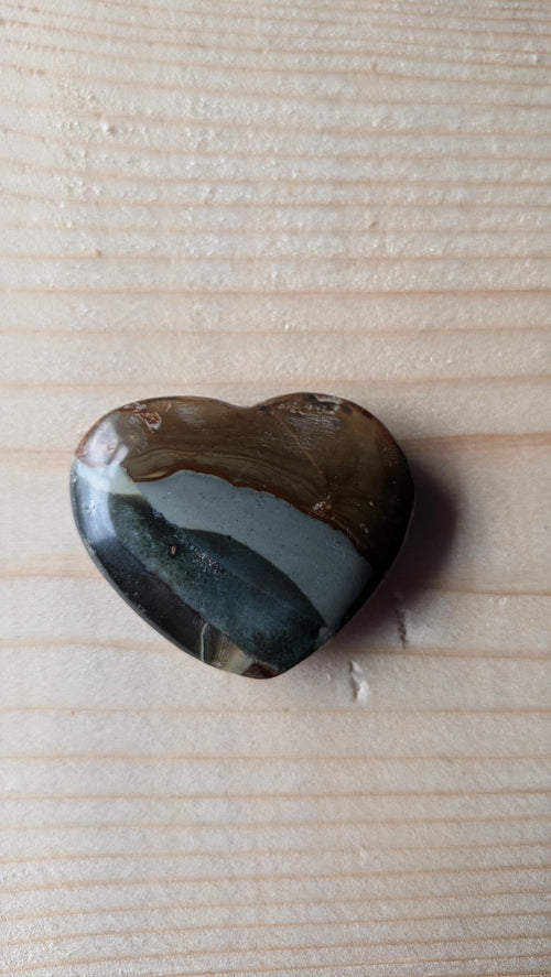Een gepolijst Oceaan Jaspis hart met duidelijke lagen van bruin, grijsblauw en donkergroen, 4,5 cm groot, op een houten ondergrond.