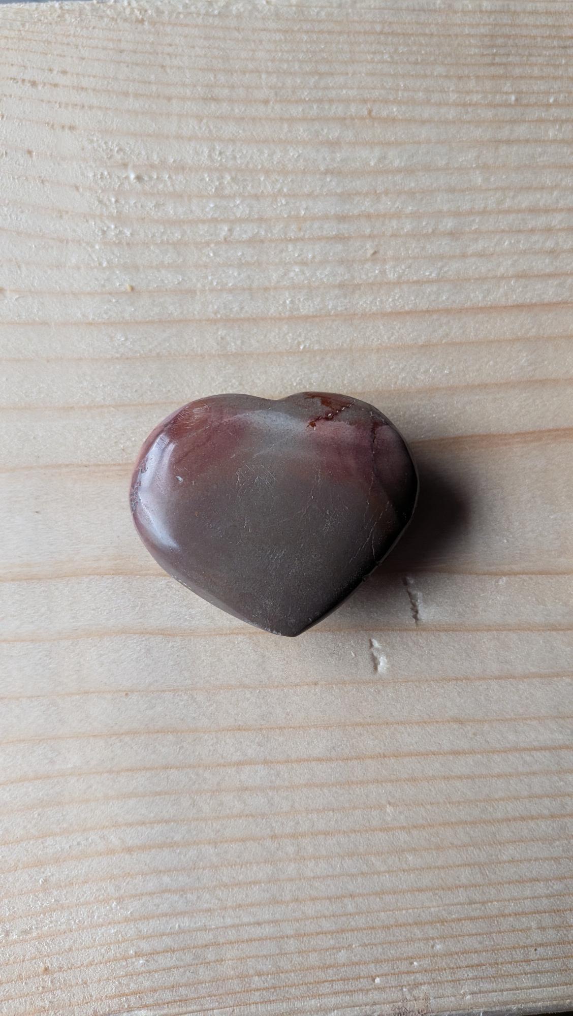 Een gepolijst hart van Polychroom Jaspis met vloeiende aardse kleuren zoals bruin, grijs en roze-rood, 4,5 cm groot, gefotografeerd op een houten achtergrond.