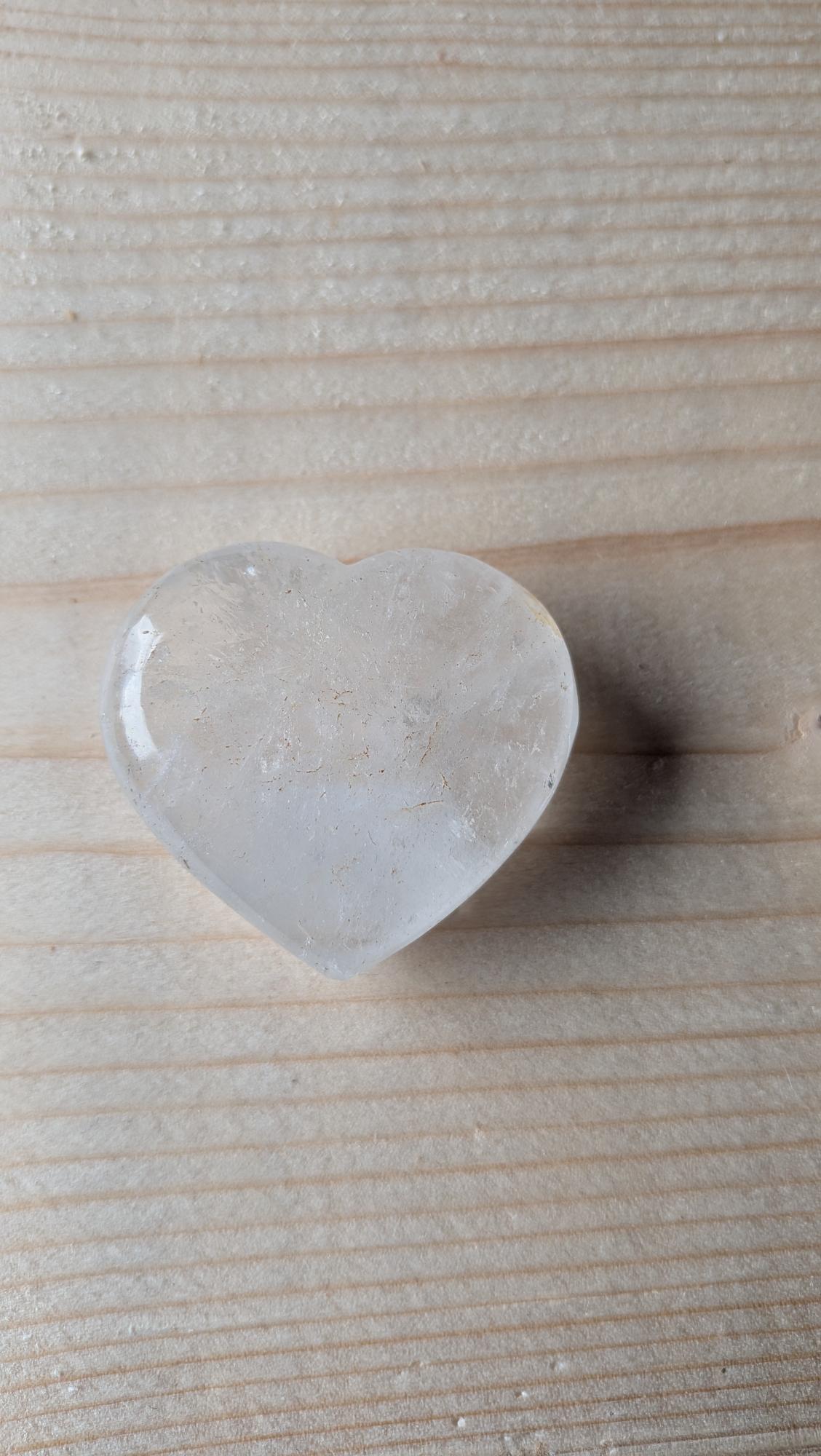 Een transparant, gepolijst Bergkristal hart met natuurlijke interne reflecties, 4 cm groot, gefotografeerd op een houten ondergrond.