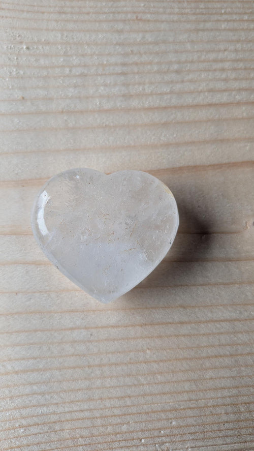 Een transparant, gepolijst Bergkristal hart met natuurlijke interne reflecties, 4 cm groot, gefotografeerd op een houten ondergrond.