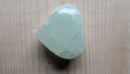 Een zachtgroen gepolijst hart van Groene Calciet met een wasachtige glans en ijzige kristalstructuur, 5 cm groot, gefotografeerd op een houten ondergrond.
