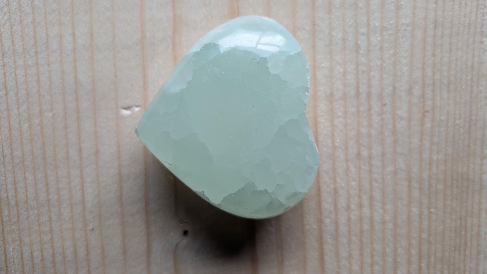 Een zachtgroen gepolijst hart van Groene Calciet met een wasachtige glans en ijzige kristalstructuur, 5 cm groot, gefotografeerd op een houten ondergrond.