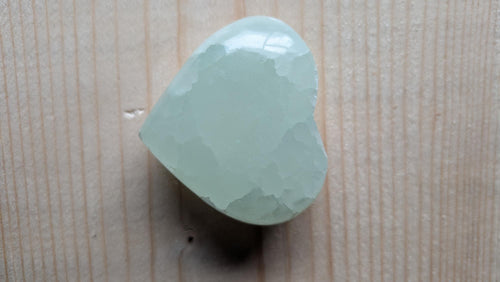 Een zachtgroen gepolijst hart van Groene Calciet met een wasachtige glans en ijzige kristalstructuur, 5 cm groot, gefotografeerd op een houten ondergrond.
