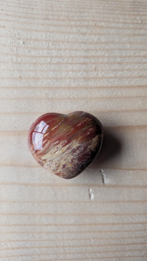Een gepolijst hartje van Versteend Hout met warme bruine en rode houtnerven, 3,5 cm groot, gefotografeerd op een houten ondergrond.