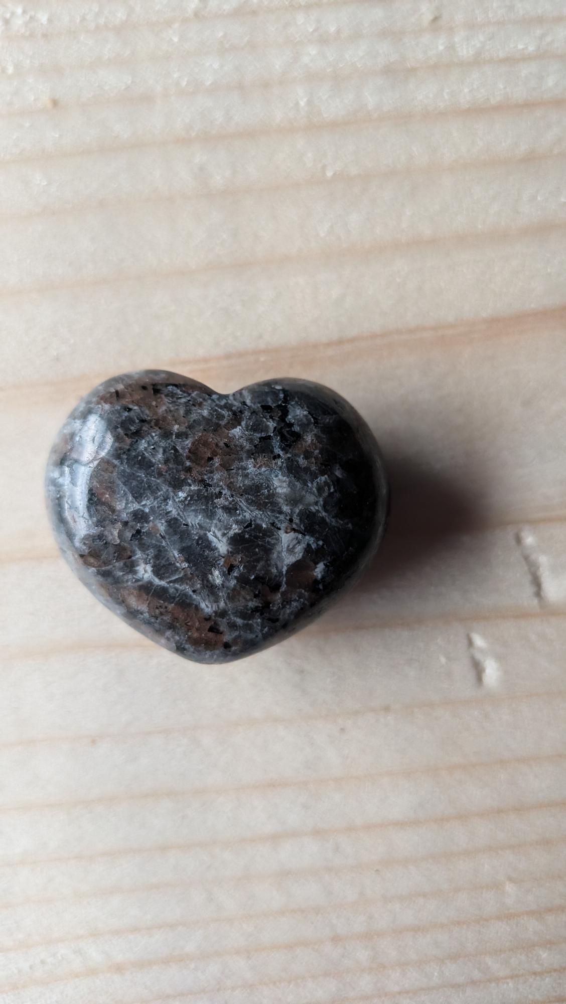 Een gepolijst grijs-zwart gespikkeld Yooperliet hartje, 3 cm groot, gefotografeerd op een houten ondergrond.