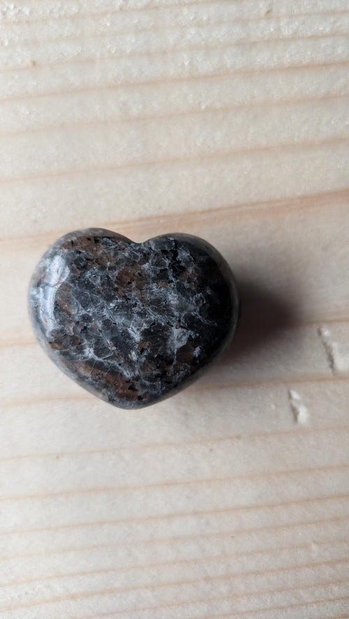 Een gepolijst grijs-zwart gespikkeld Yooperliet hartje, 3 cm groot, gefotografeerd op een houten ondergrond.