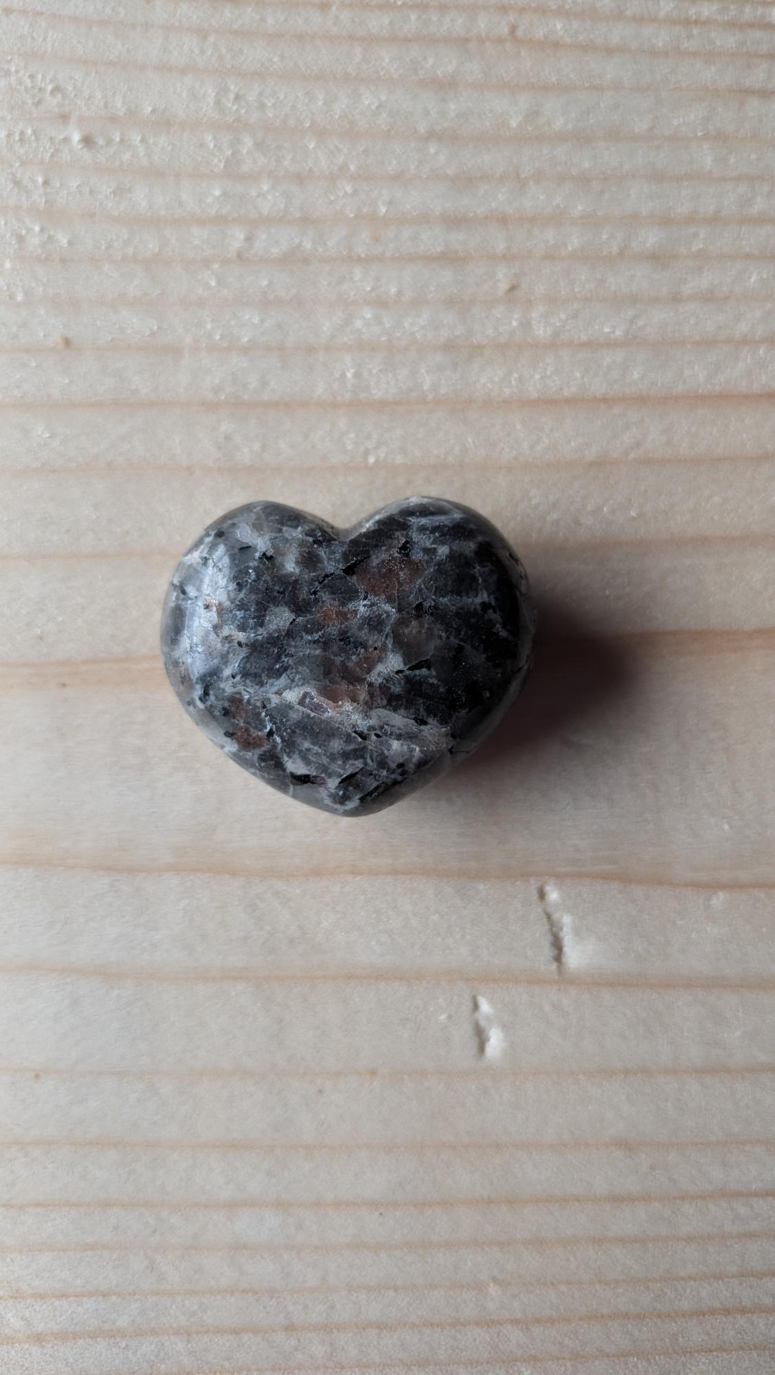 Een gepolijst hartje van grijs-zwart gespikkeld Yooperliet, 3 cm groot, gefotografeerd op een houten achtergrond.