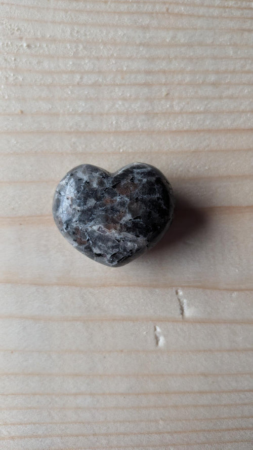 Een gepolijst hartje van grijs-zwart gespikkeld Yooperliet, 3 cm groot, gefotografeerd op een houten achtergrond.