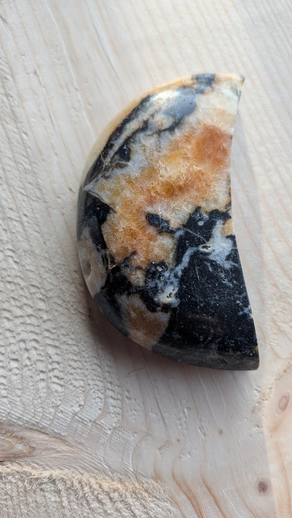 Orca Agaat maan met zwart, wit en amberkleurig patroon, 9 cm hoog op een houten ondergrond.