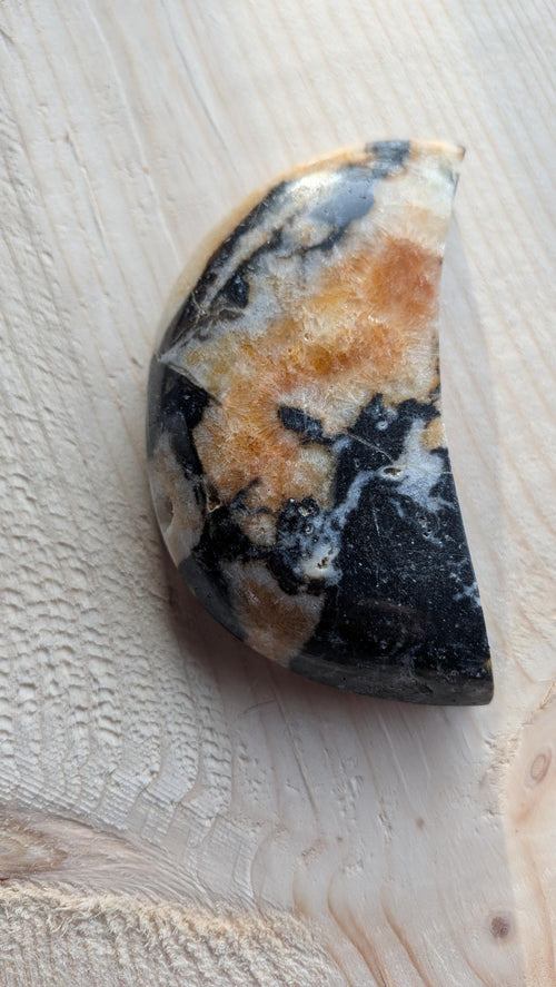 Orca Agaat maan met zwart, wit en amberkleurig patroon, 9 cm hoog op een houten ondergrond.