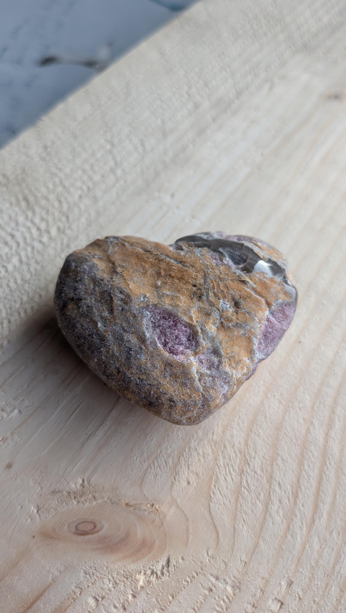 Natuurlijk hartje van robijn in matrix met paarse kleuraccenten op een lichte houten ondergrond.