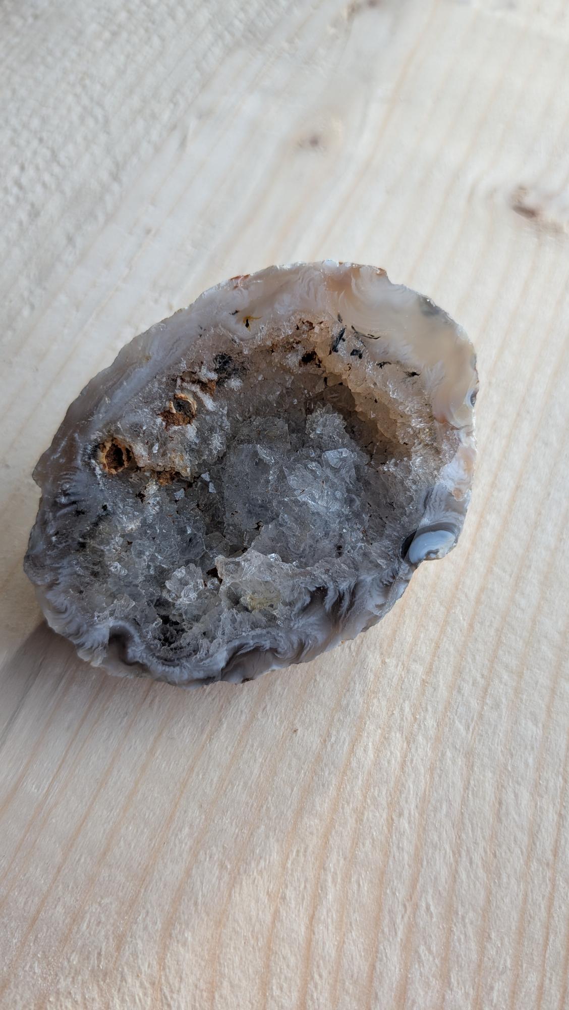 Een geopende kleine agaat geode met fonkelende kristallen van binnen op een houten ondergrond.