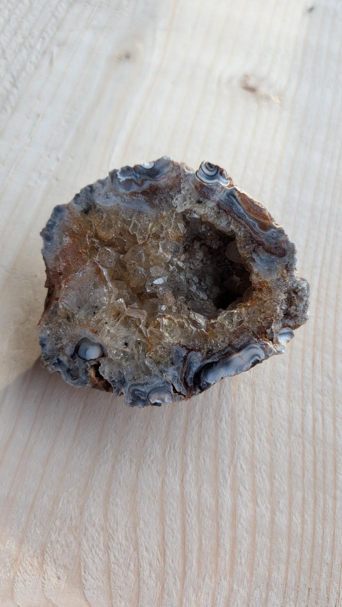 Natuurlijke agaat geode met goudbruine rookkwarts kristallen op een houten achtergrond.