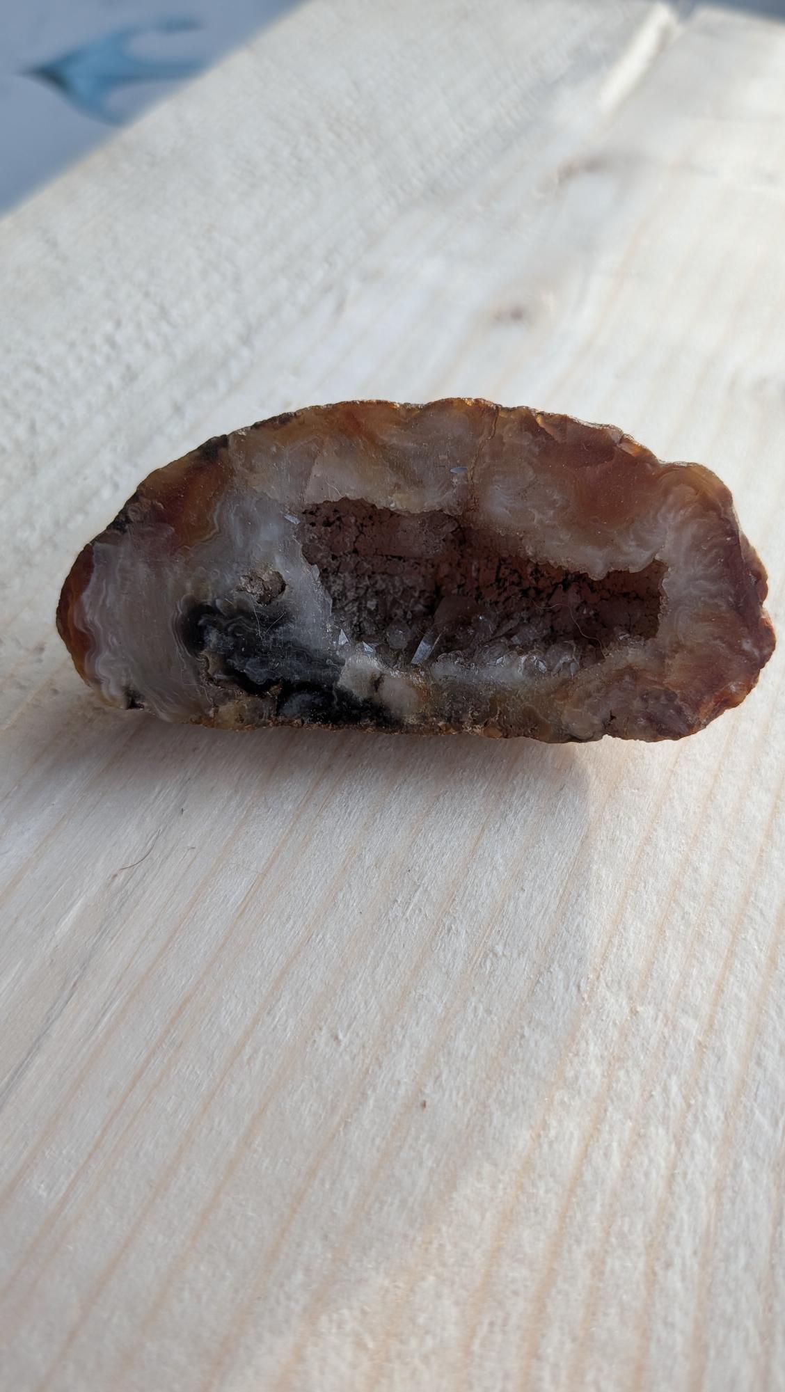 Slanke natuurlijke agaat geode van 6 cm met fonkelende kristallen op een houten achtergrond.