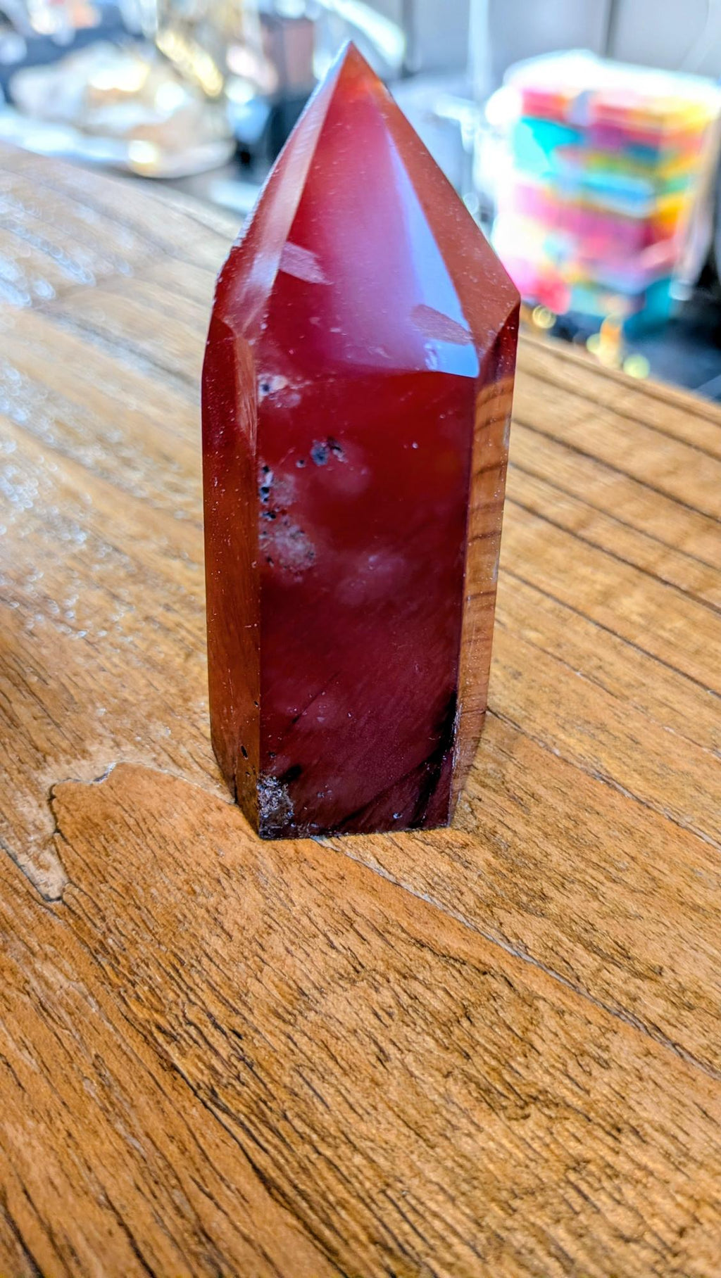 "Vooraanzicht van een dieprode, gepolijste carneool toren van 9 cm hoog op een houten ondergrond."