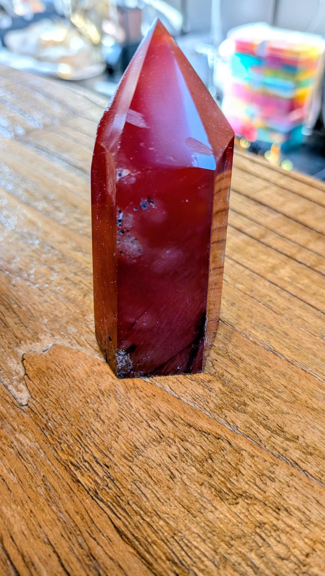 "Vooraanzicht van een dieprode, gepolijste carneool toren van 9 cm hoog op een houten ondergrond."