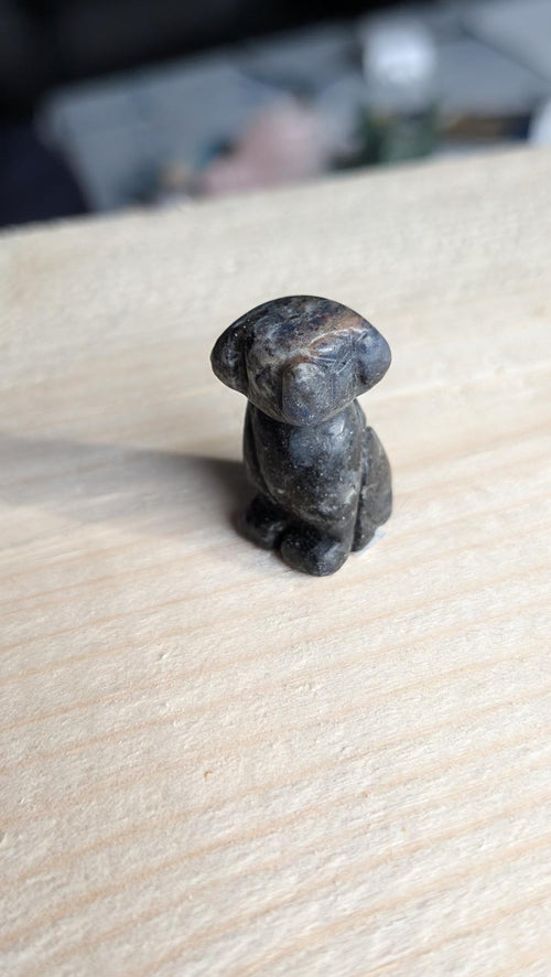 Handgesneden miniatuur hondje van donkerblauwe sodaliet edelsteen op een houten ondergrond.