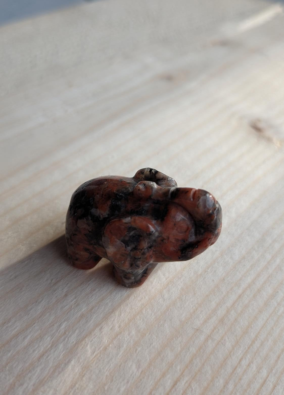 Handgesneden olifantje van roodbruine en zwarte mahonie obsidiaan op een houten ondergrond.