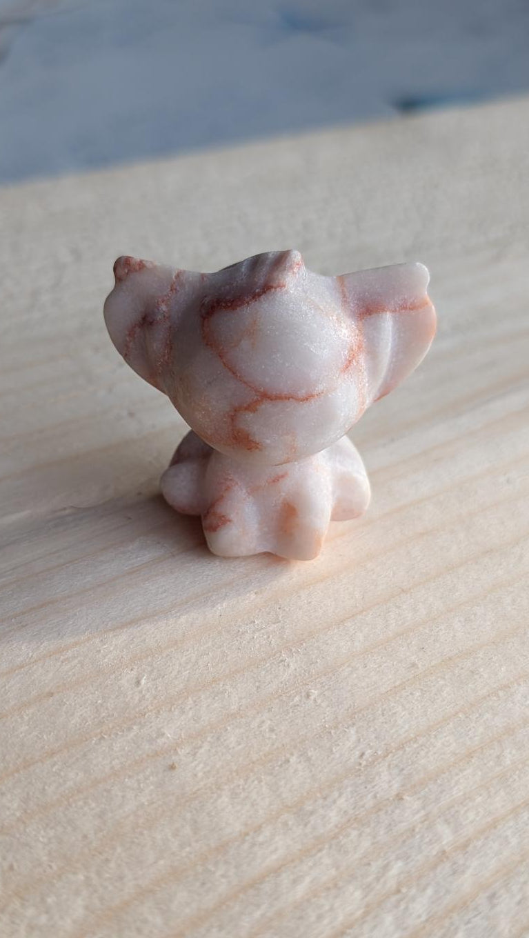 Handgesneden Stitch figuurtje van zandkleurige landschapsjaspis met bruine lijnen op een houten achtergrond.