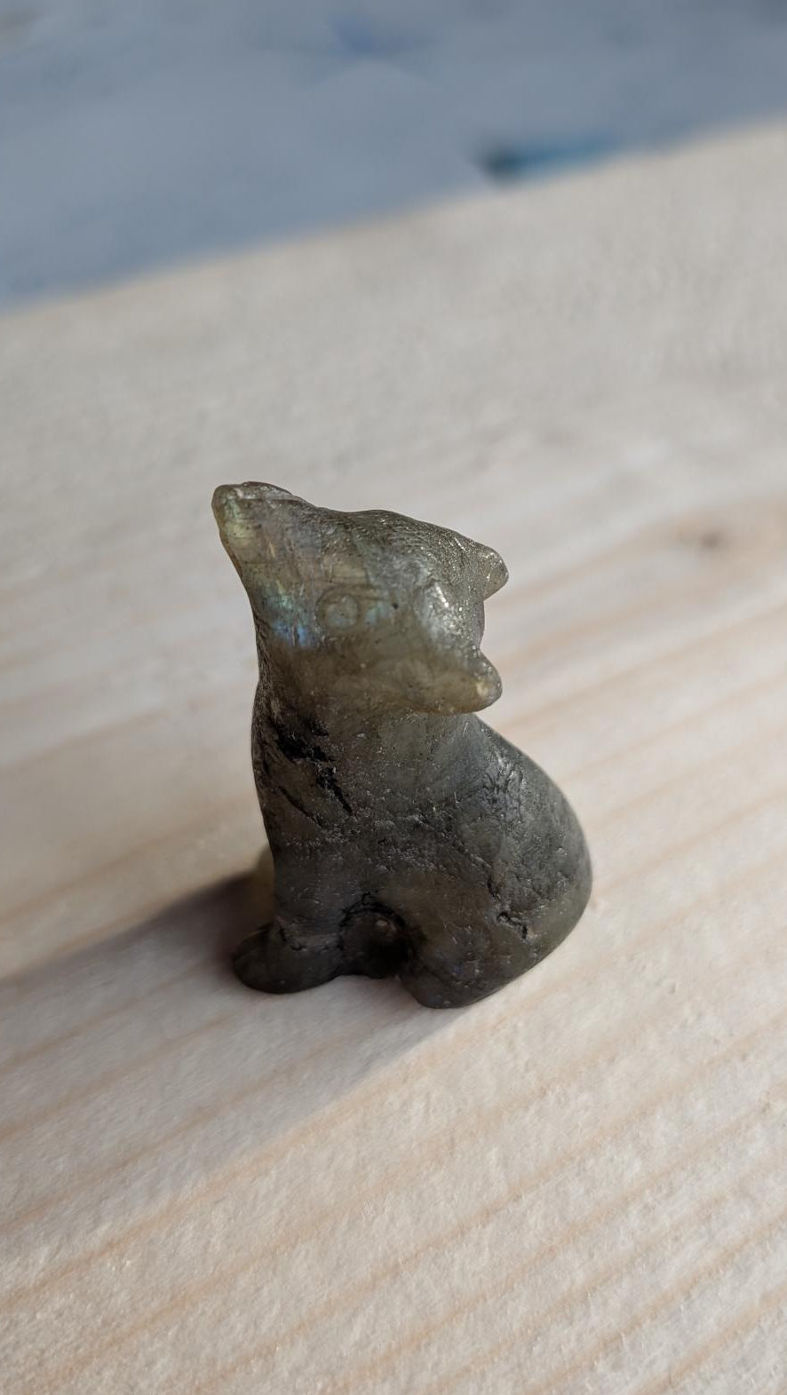 andgesneden wolfje van grijze labradoriet met blauwe glans op een houten ondergrond.