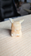 Handgesneden Pikachu figuurtje van gele calciet edelsteen op een houten achtergrond.
