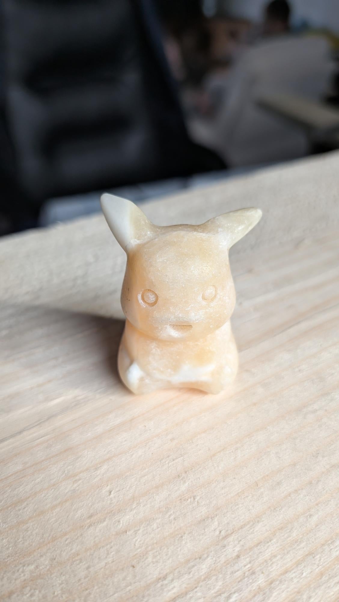 Handgesneden Pikachu figuurtje van gele calciet edelsteen op een houten achtergrond.