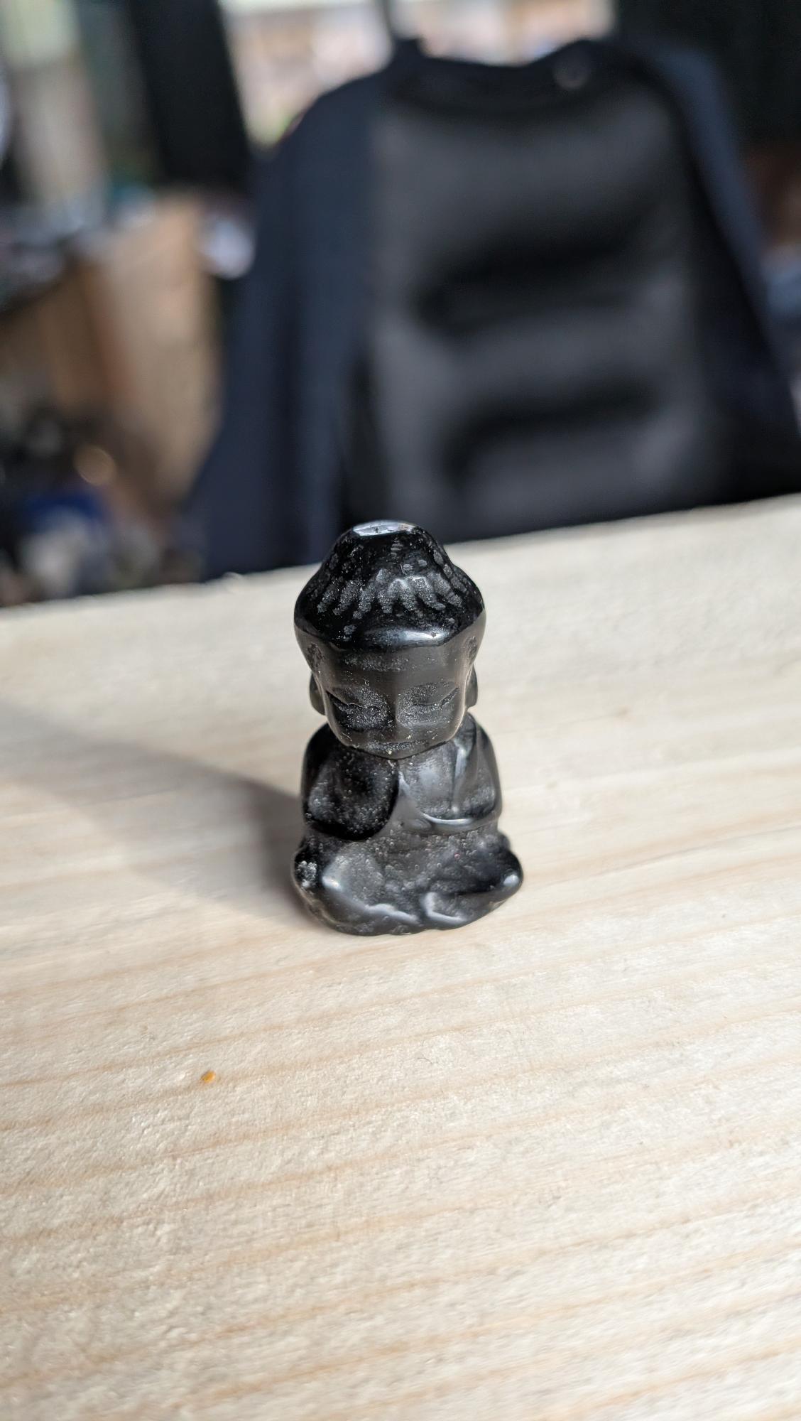 Handgesneden mini Boeddha van gitzwarte obsidiaan op een houten achtergrond.