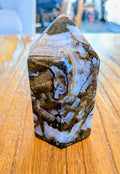 "Gepolijste Mozaïek Chalcedoon toren met complexe patronen van wit kristal en bruine matrix op een houten tafel."