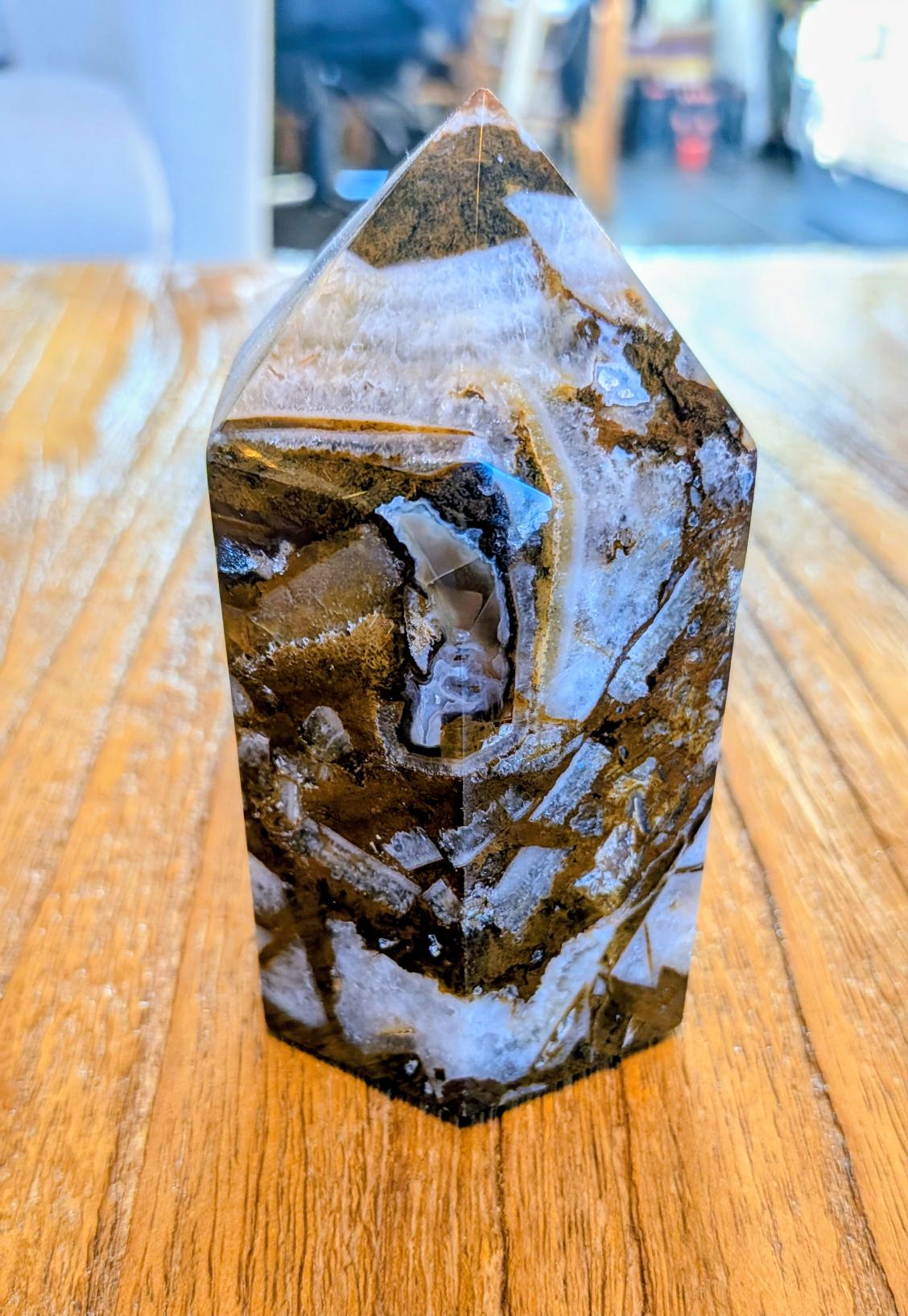 "Gepolijste Mozaïek Chalcedoon toren met complexe patronen van wit kristal en bruine matrix op een houten tafel."