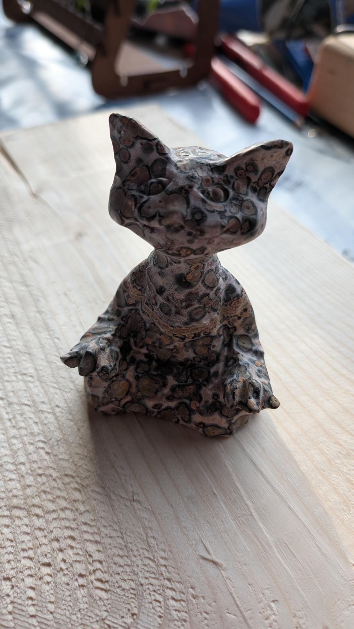 Grote handgesneden kat van luipaard jaspis met uniek vlekkenpatroon op een houten ondergrond.
