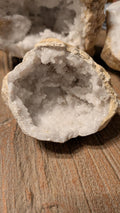 Opengewerkte witte kristalgeode met schitterende kristallen binnenin, liggend op een houten ondergrond.