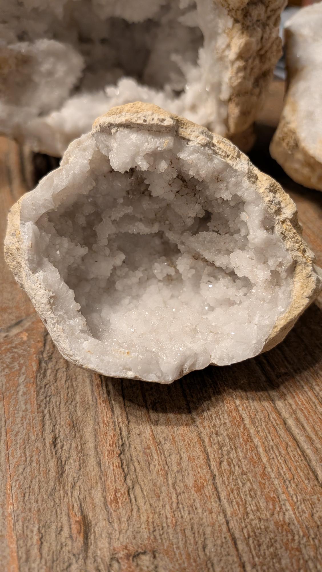 Opengewerkte witte kristalgeode met schitterende kristallen binnenin, liggend op een houten ondergrond.