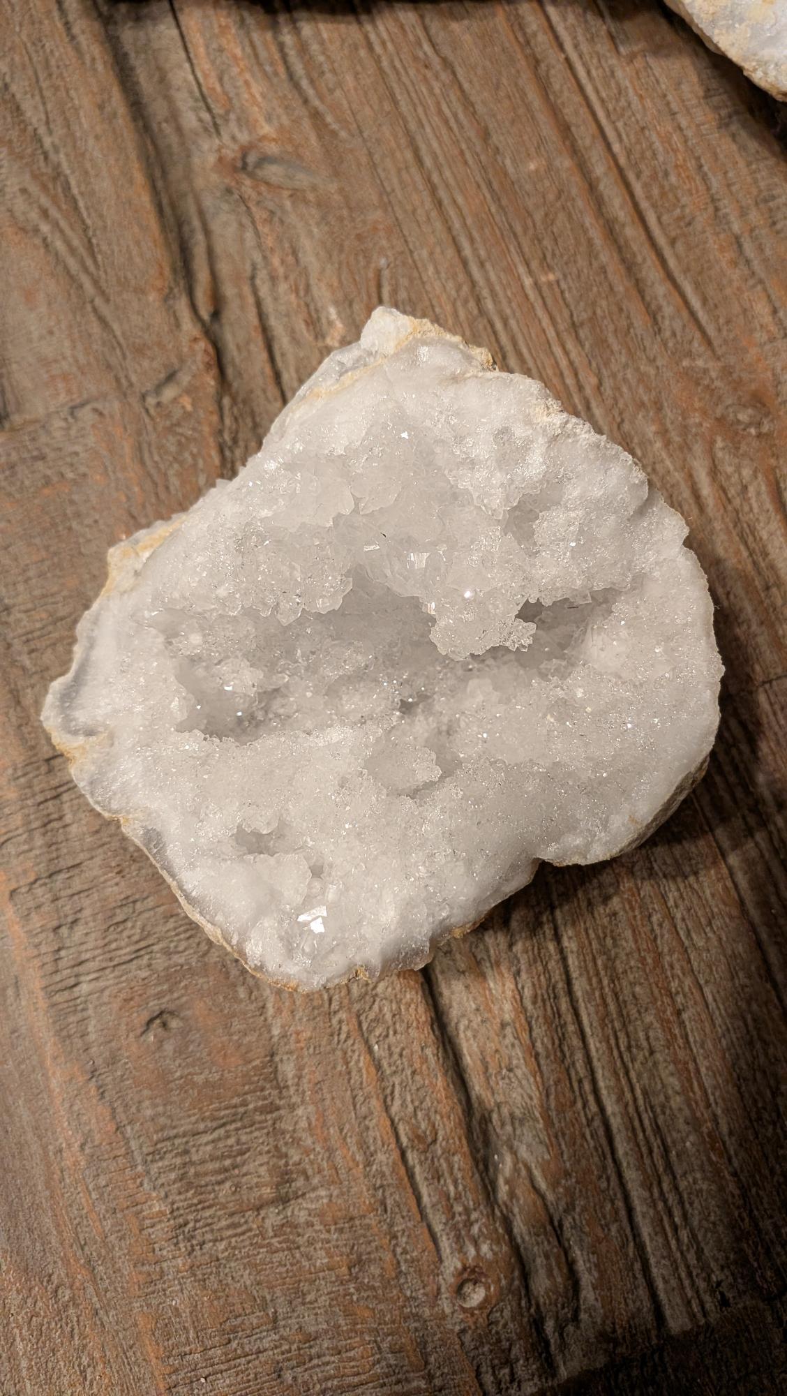 Grote opengebroken kristalgeode van 400 gram met witte glinsterende kristallen, gefotografeerd op een rustieke houten tafel.